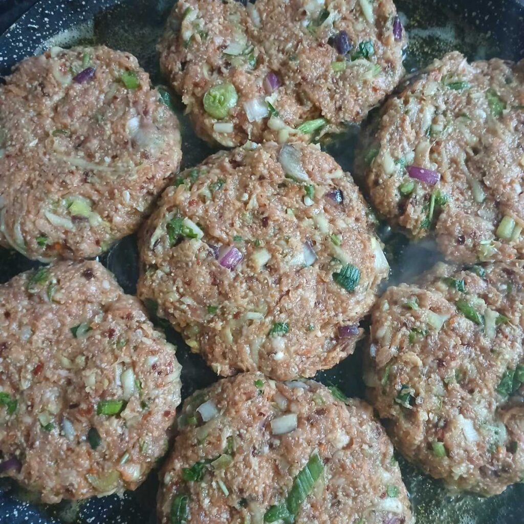 Raw mixture for Zucchini Carrot Beef Patties shaped into round patties and arranged in a pan before cooking.