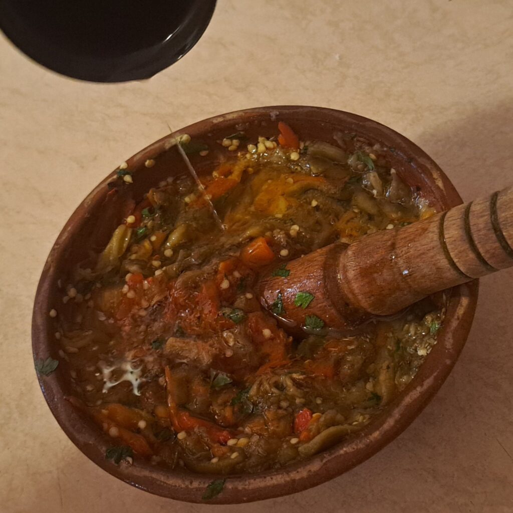 Clay bowl filled with pounded eggplant, peppers, garlic, parsley, ready for hot oil pouring.