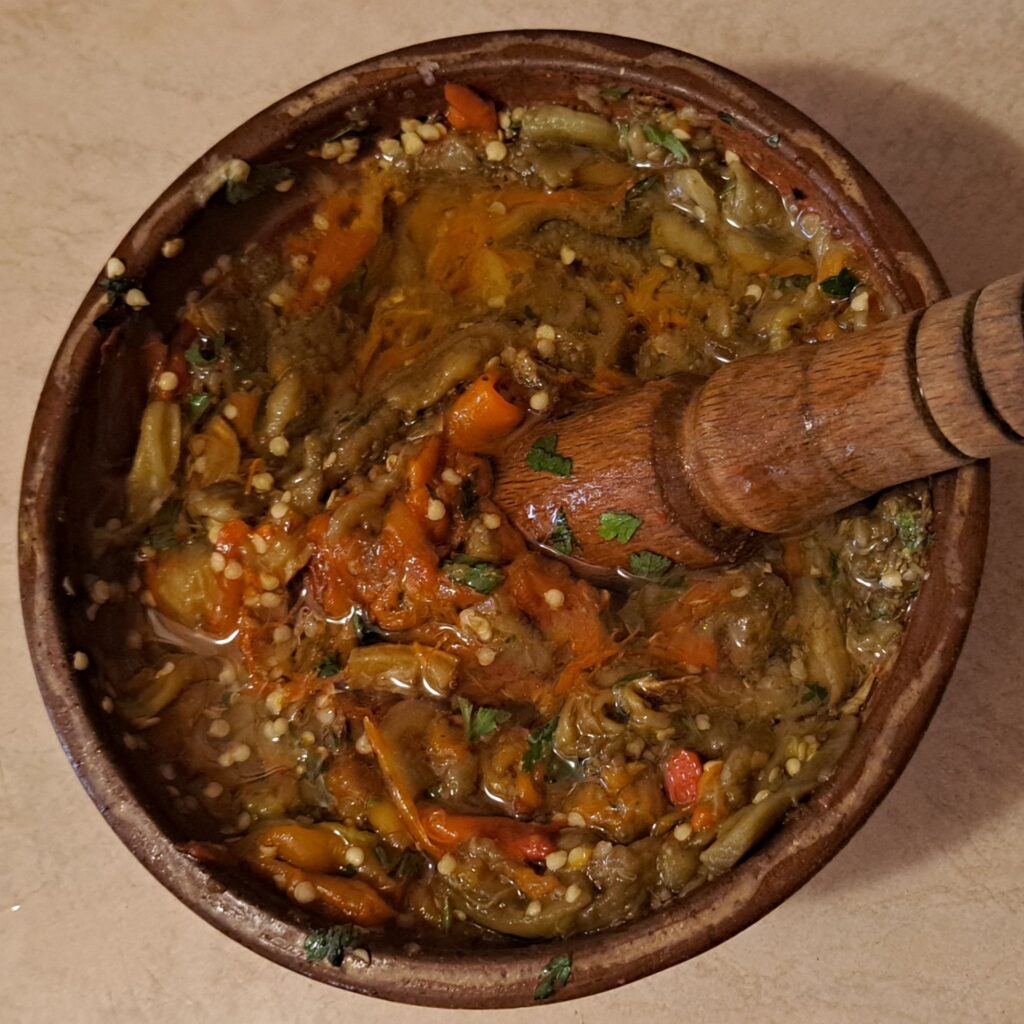 Clay bowl filled with fully prepared pounded eggplant, peppers, garlic, and parsley, ready to enjoy.