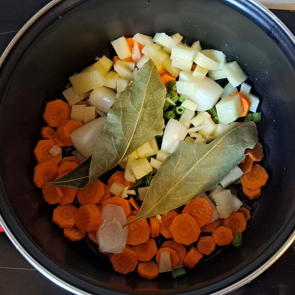 Chopped carrots, onion, celery, potato and bay leaves in a pot with oil.