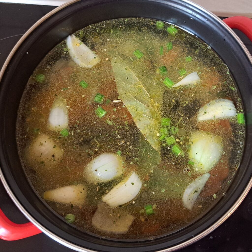 Soup base boiling in pot with water and dried seasoning.