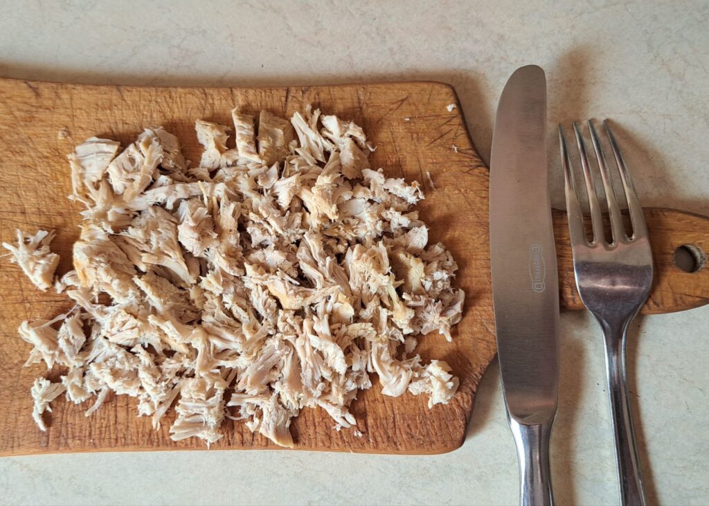Finely chopped boiled chicken on cutting board ready for soup.
