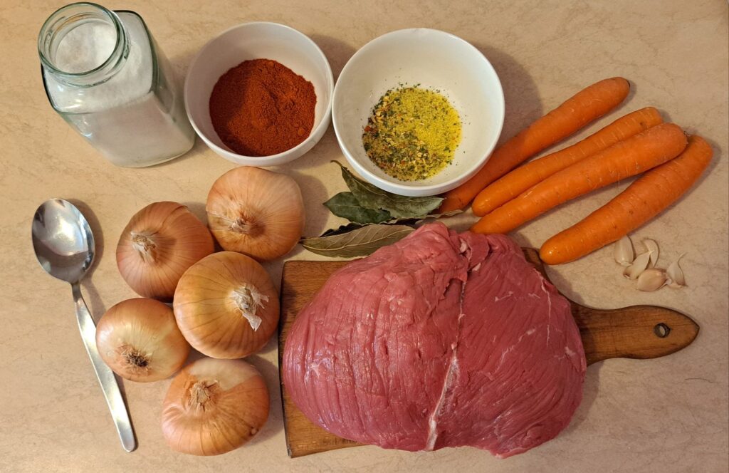 Whole ingredients for Beef Goulash including beef, onions, carrots, garlic, paprika, and bay leaves.