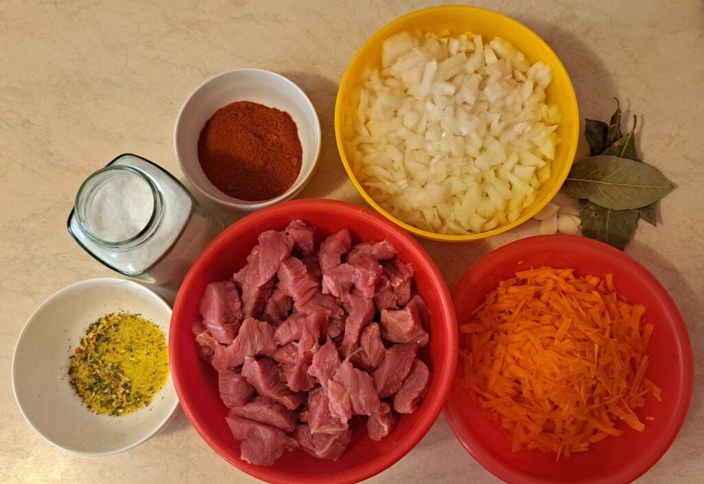 Beef cut into pieces, chopped onions, grated carrots, paprika, garlic, bay leaves, and seasoning.
