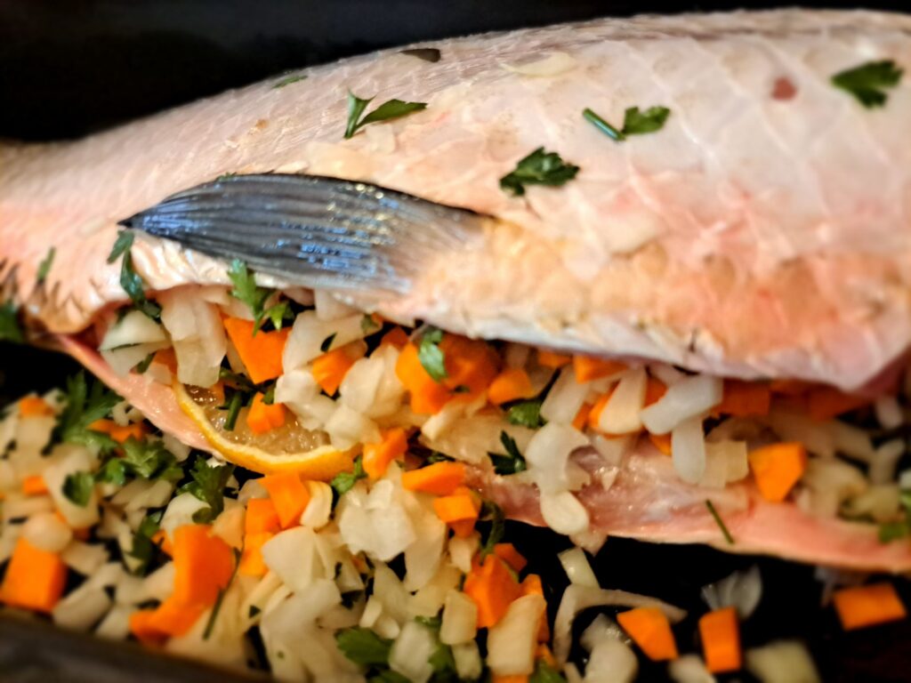 Whole carp stuffed with lemon, onions, garlic, carrots, eggplant, parsley, with remaining vegetables placed around it directly in the baking tray.