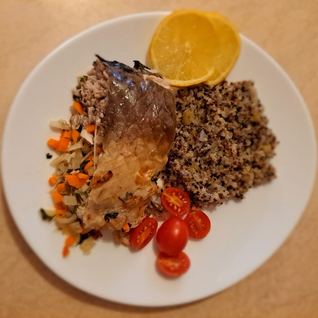 Full view of stuffed carp served with quinoa, cherry tomatoes, and lemon slices in a home dining setting.