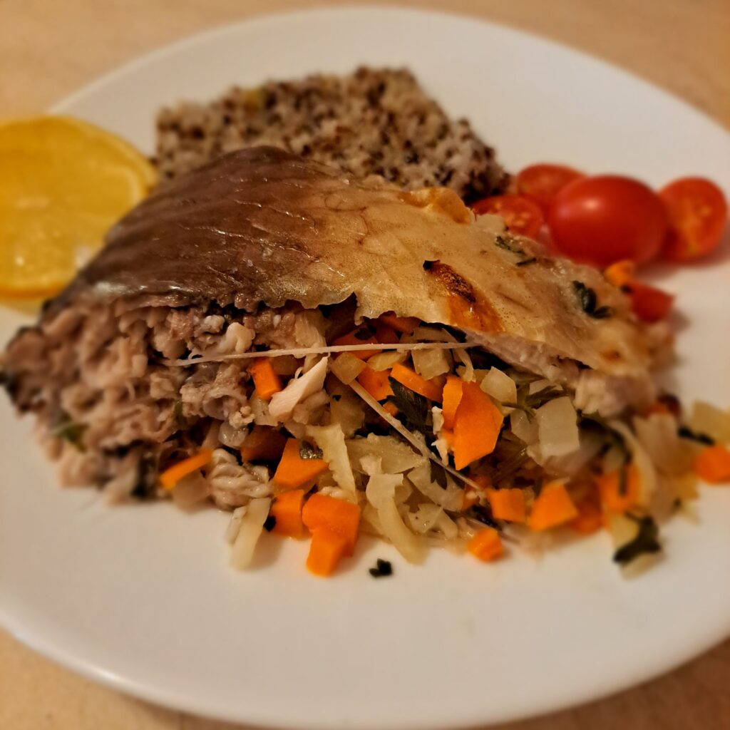 Close-up of a cut piece of stuffed carp served with mixed quinoa, cherry tomatoes, and lemon slices on plate.