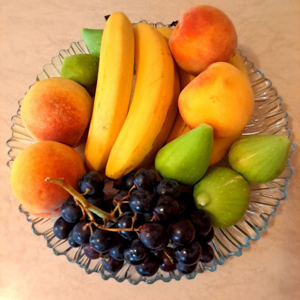 Whole fresh fruits including peach, figs, banana, and grapes arranged on a plate for carpaccio.