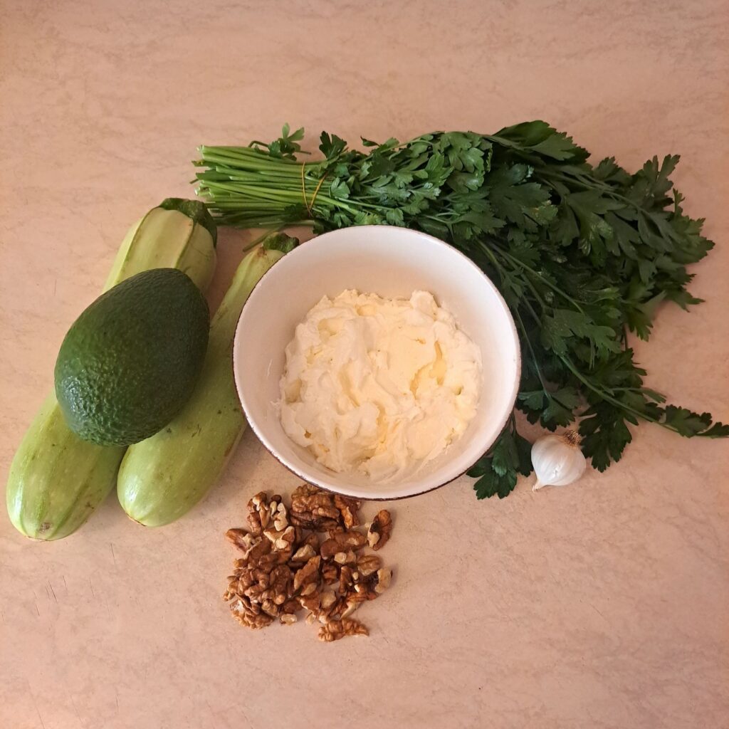Fresh zucchini, avocado, cream cheese, walnuts, garlic, and parsley arranged for the recipe.