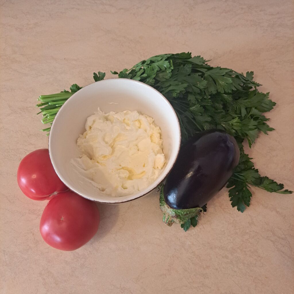 Fresh eggplant, tomatoes, and ricotta cheese arranged together for the recipe.