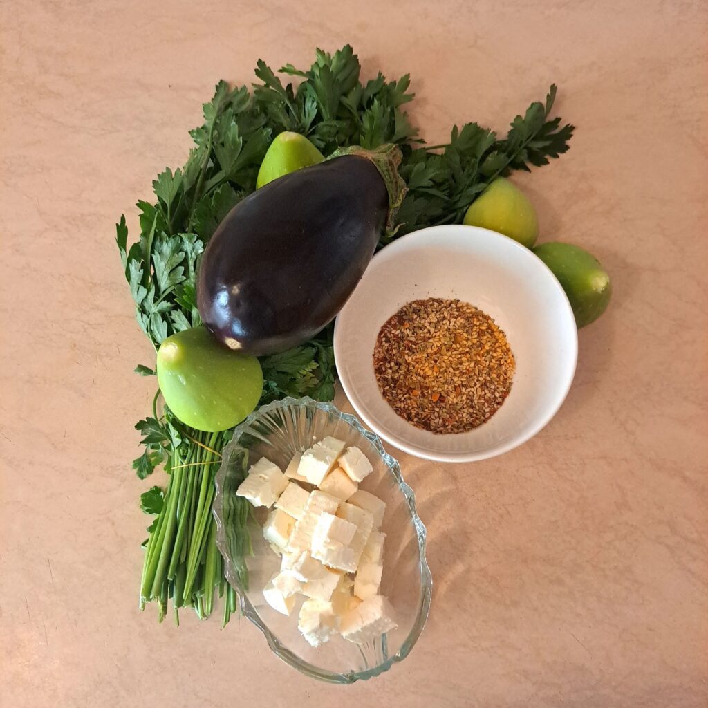 Fresh eggplant, figs, feta cheese, za’atar spice, and parsley arranged for the recipe.
