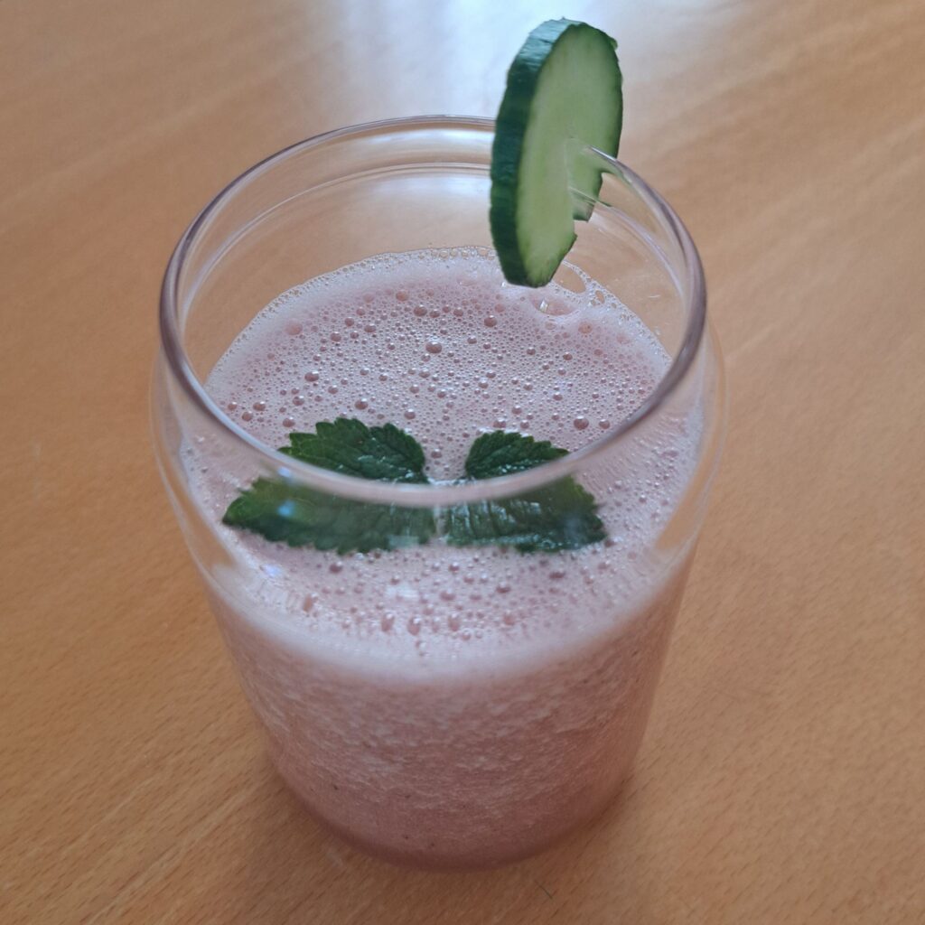 Side view of watermelon cucumber mint juice in a glass, garnished with cucumber slice and mint leaves.