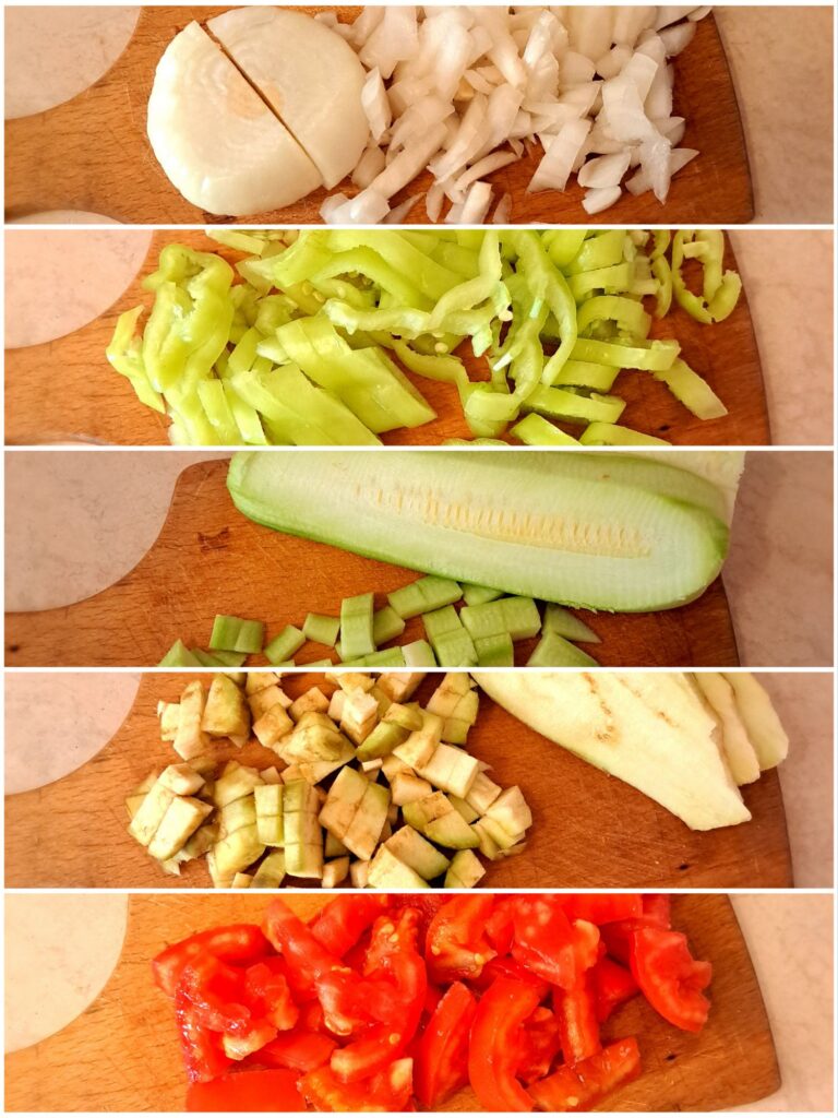 Finely chopped onions, peppers, tomatoes, zucchini, and eggplant arranged on a cutting board ready for cooking.