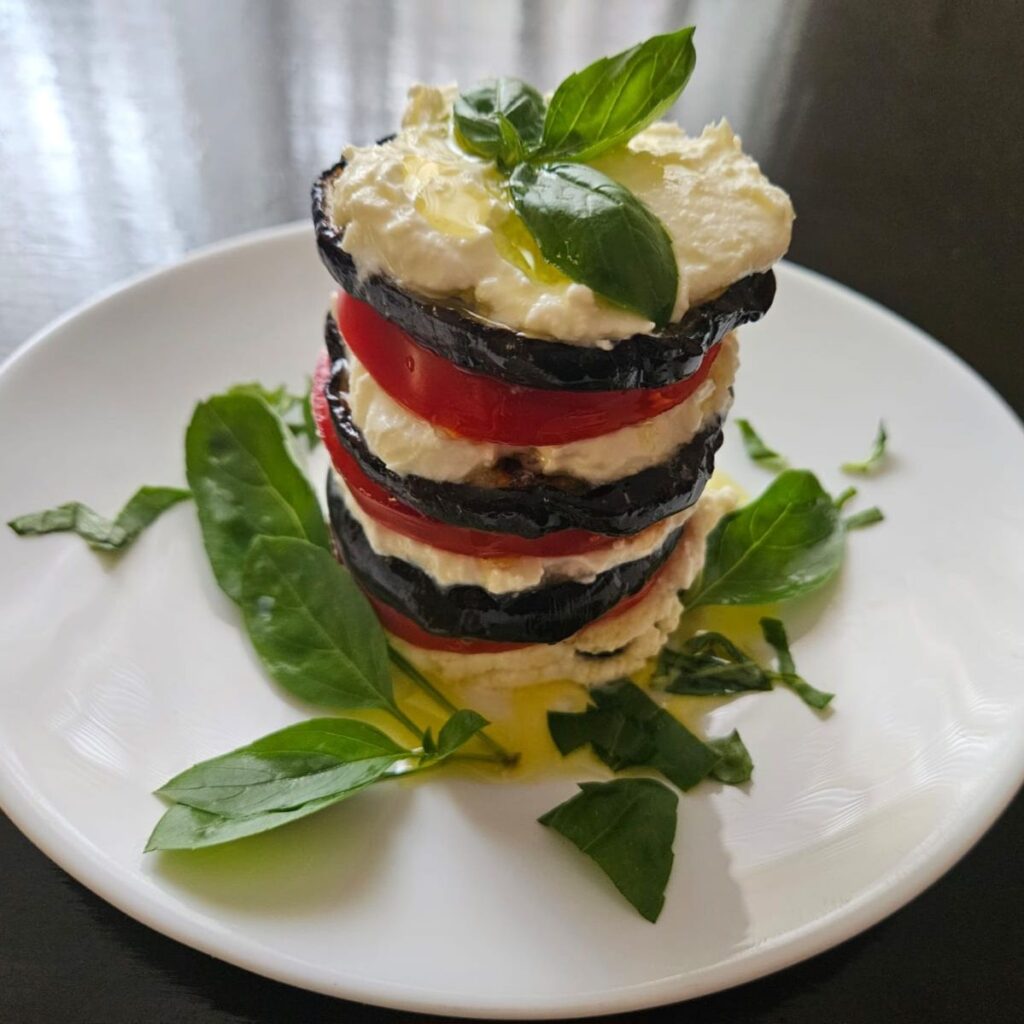 Grilled eggplant stacks layered with ricotta cheese and tomato, garnished with fresh basil.