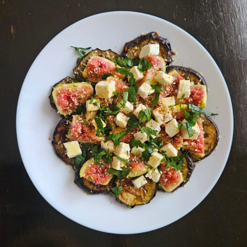Overhead view of grilled eggplant and fig salad with feta cheese, served in a white plate.