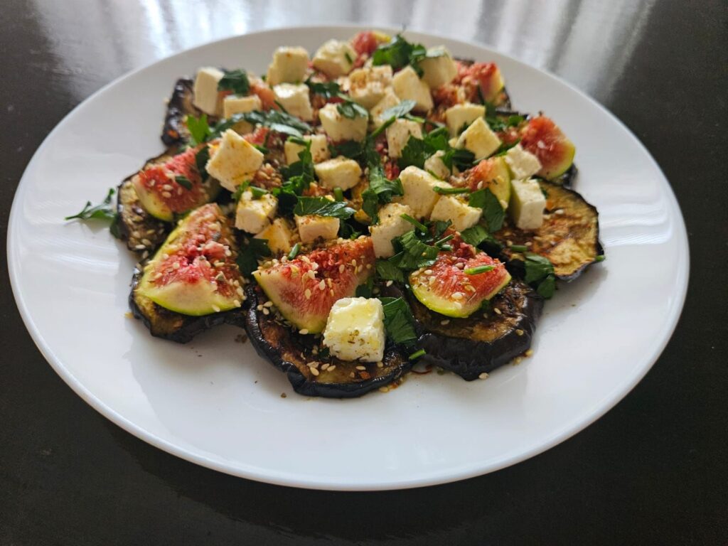 Grilled eggplant and fig salad with feta served in a white plate, photographed from the side.