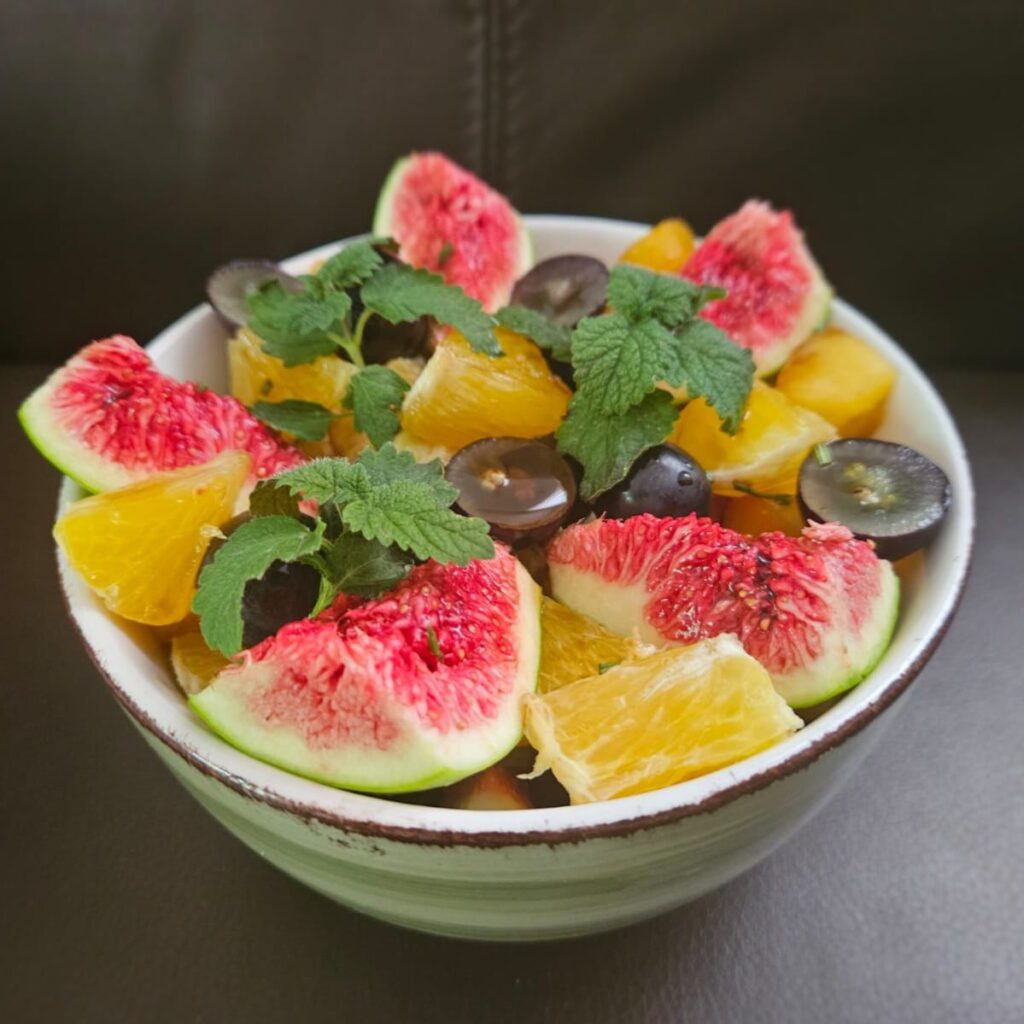 Side view close-up of elegant fruit salad in a rounded bowl, showing colorful layers of fruit and mint.
