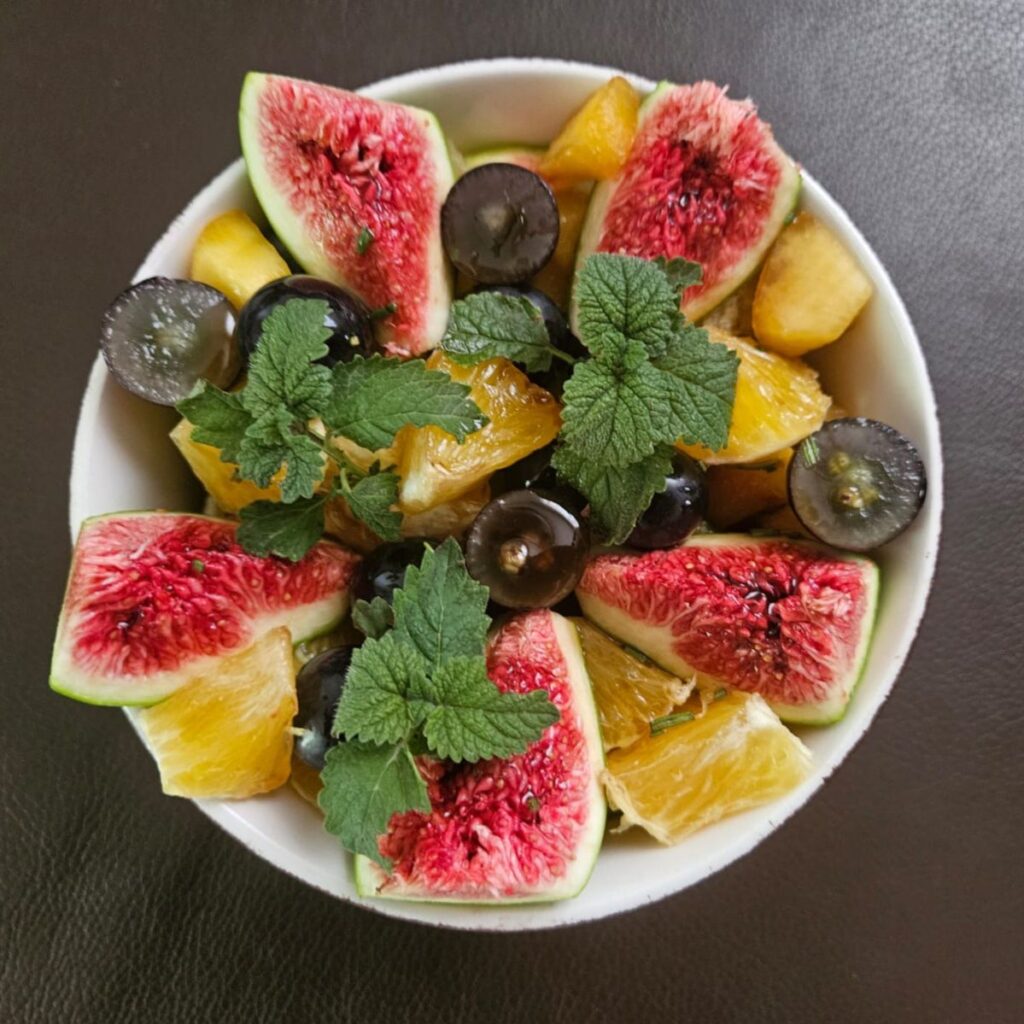 Overhead view of elegant fruit salad served in a tall rounded bowl with fresh garnish.