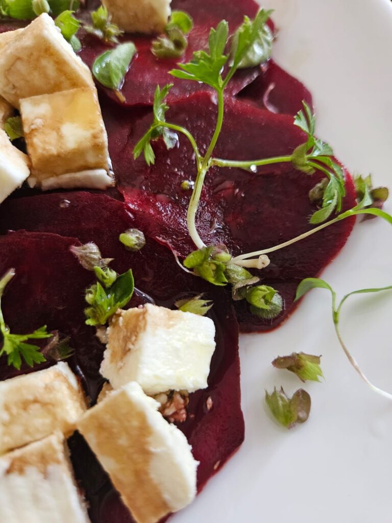 Overhead close-up of beet carpaccio with feta and microgreens served on a plate.