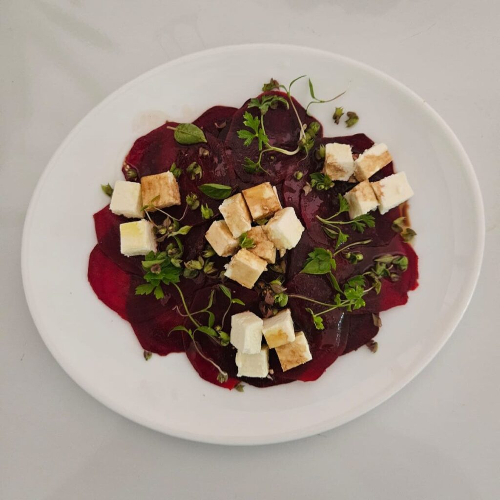 Full plate of beet carpaccio topped with feta and microgreens, photographed from above.
