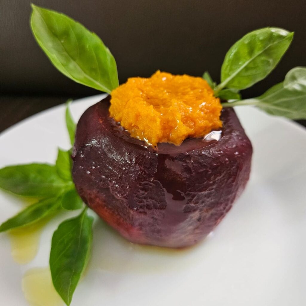 Close-up of stuffed roasted beetroot with sweet potato puree, garnished with basil leaves and olive oil.