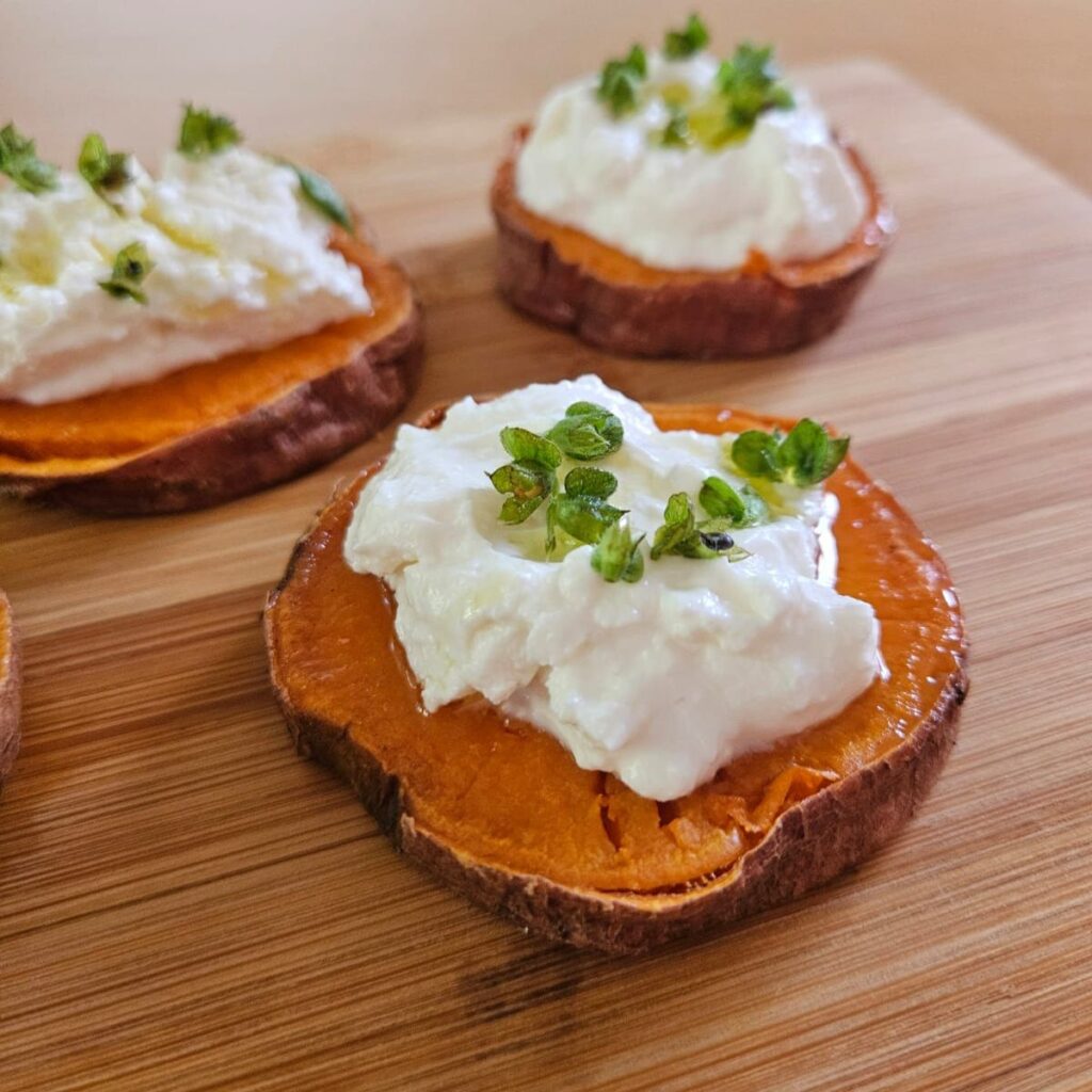 Close-up of sweet potato bites topped with ricotta and microgreens, served on a wooden board.