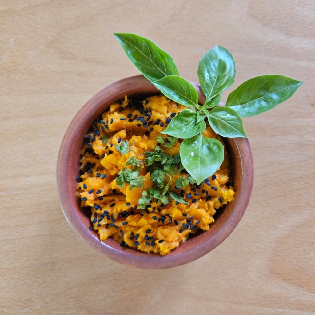 Served sweet potato mash topped with black sesame, microgreens, and basil leaves in a ceramic bowl.