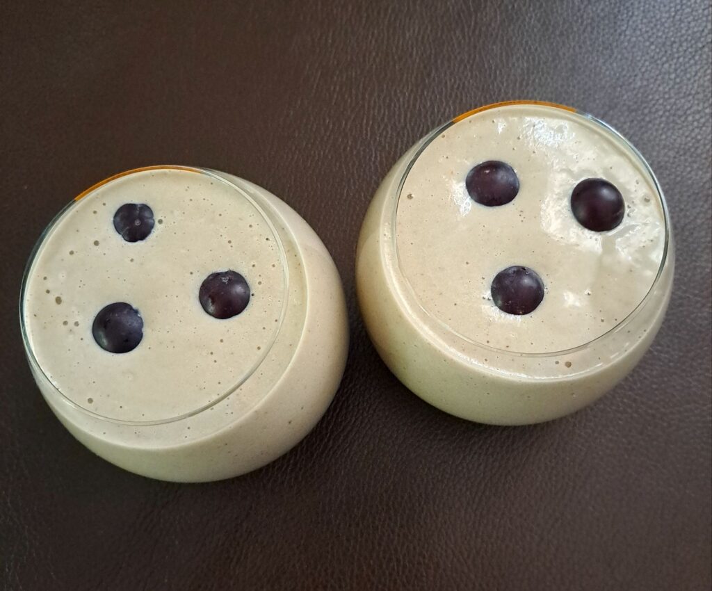 Two low rounded glasses with Baobab Avocado Banana Smoothie, each topped with three grapes for decoration.