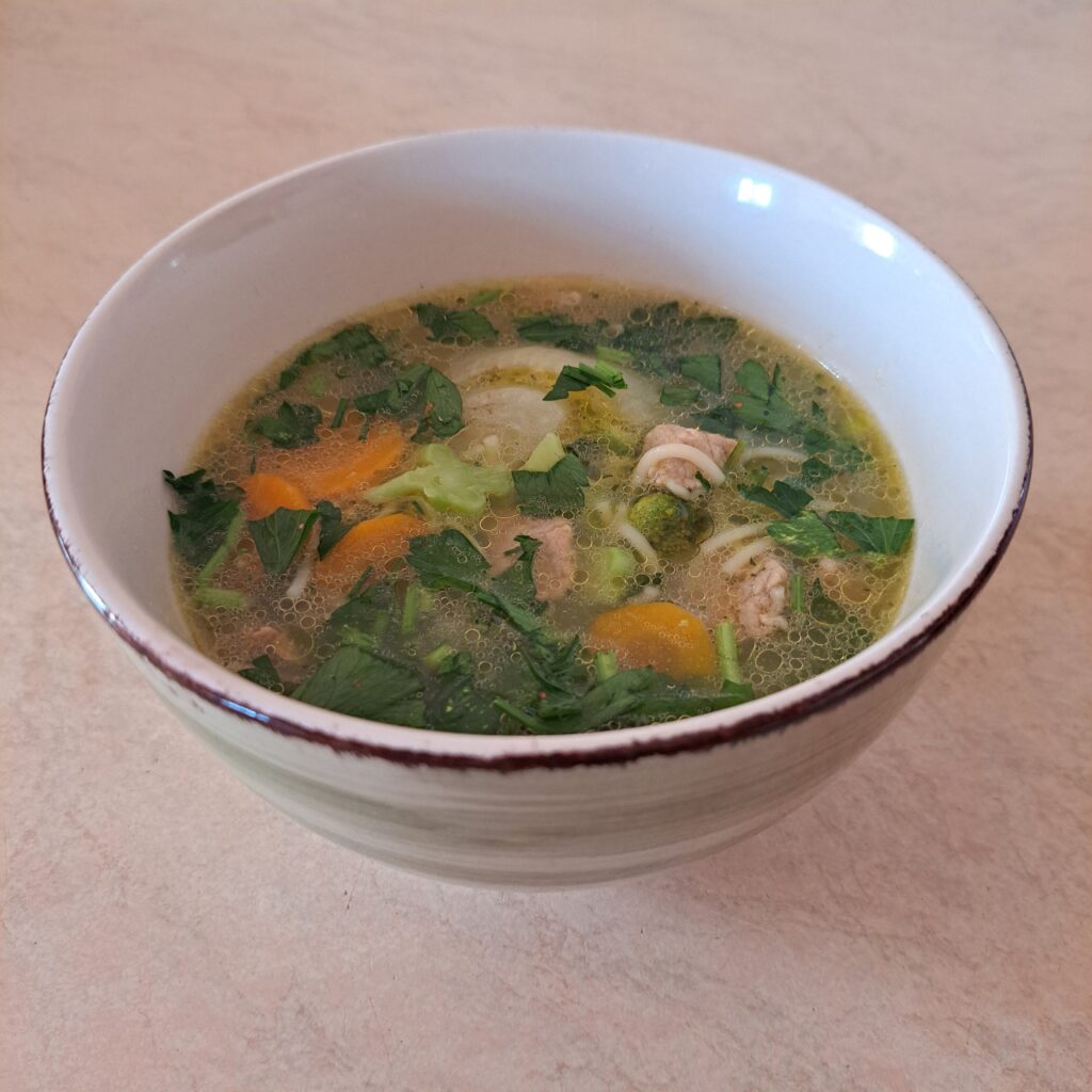 Side view of Pork Vegetable Noodle Soup in a bowl, garnished with fresh parsley, ready to enjoy.