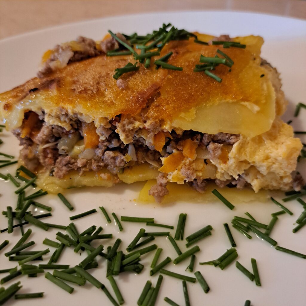 Close-up side view of a single portion of potato zucchini meat moussaka with fresh chives.
