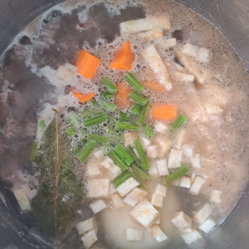 All ingredients simmering in a pot, including beef, parsnip, celery, carrot, onion, garlic, and bay leaf.