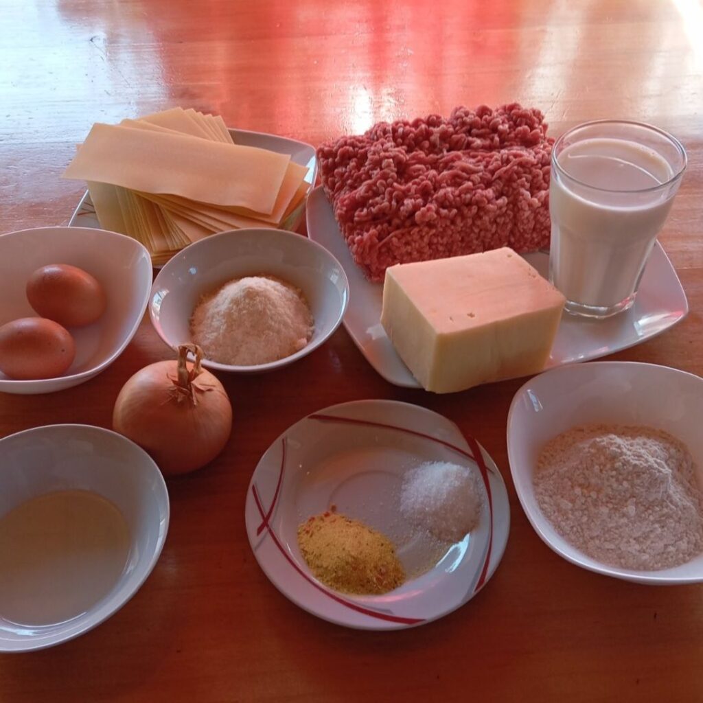 All ingredients for Homemade Meat Bechamel Lasagna arranged on a kitchen table.