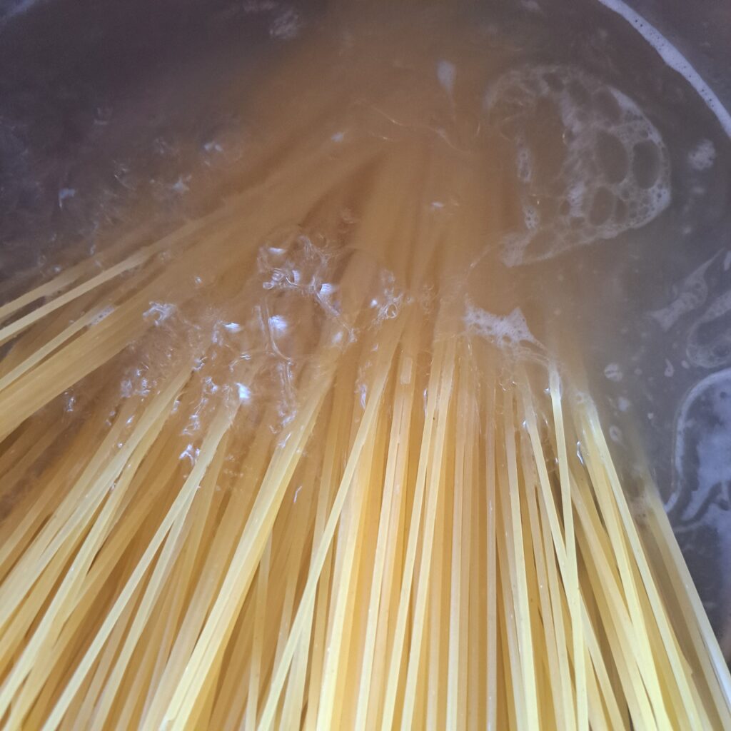 Close-up of a pot with boiling water where spaghetti is cooking at the beginning of preparation.