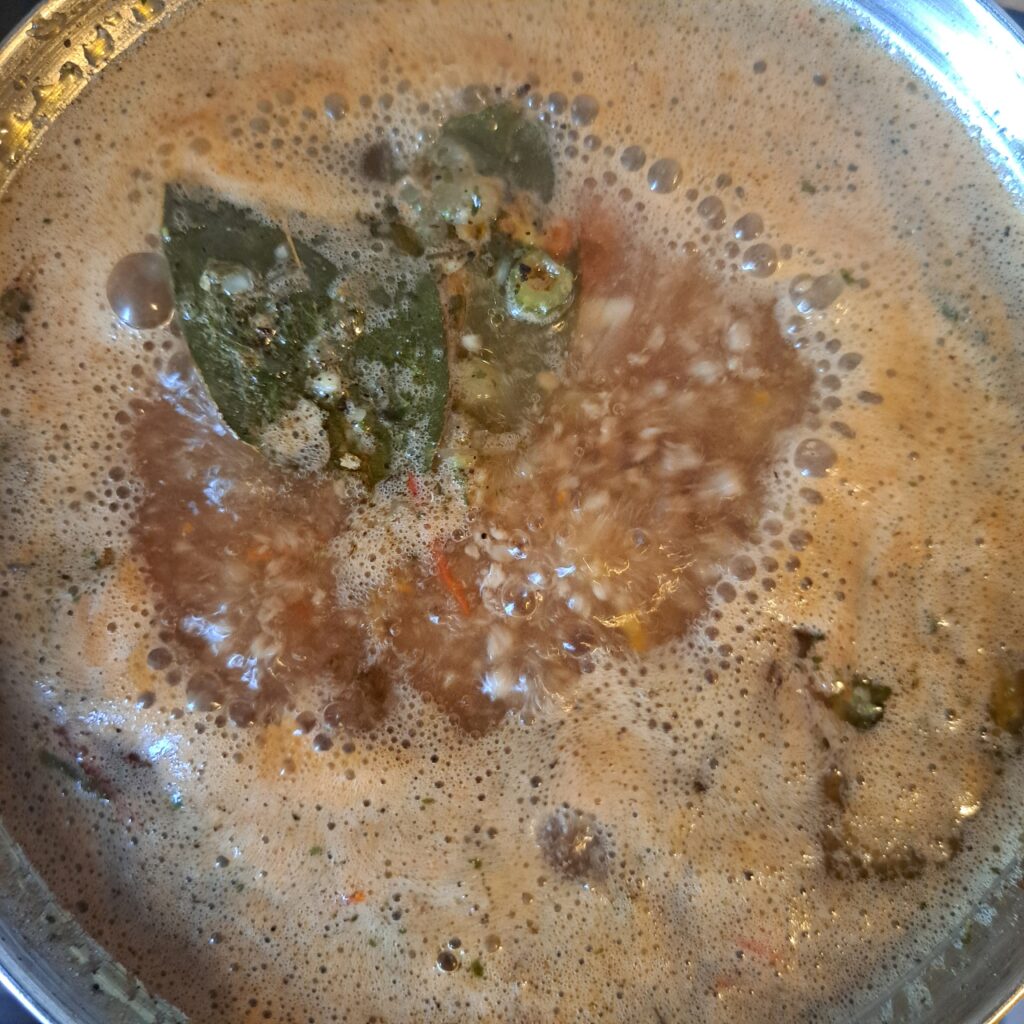 Pot with all ingredients boiling, including vegetables, meat, and macaroni for soup.