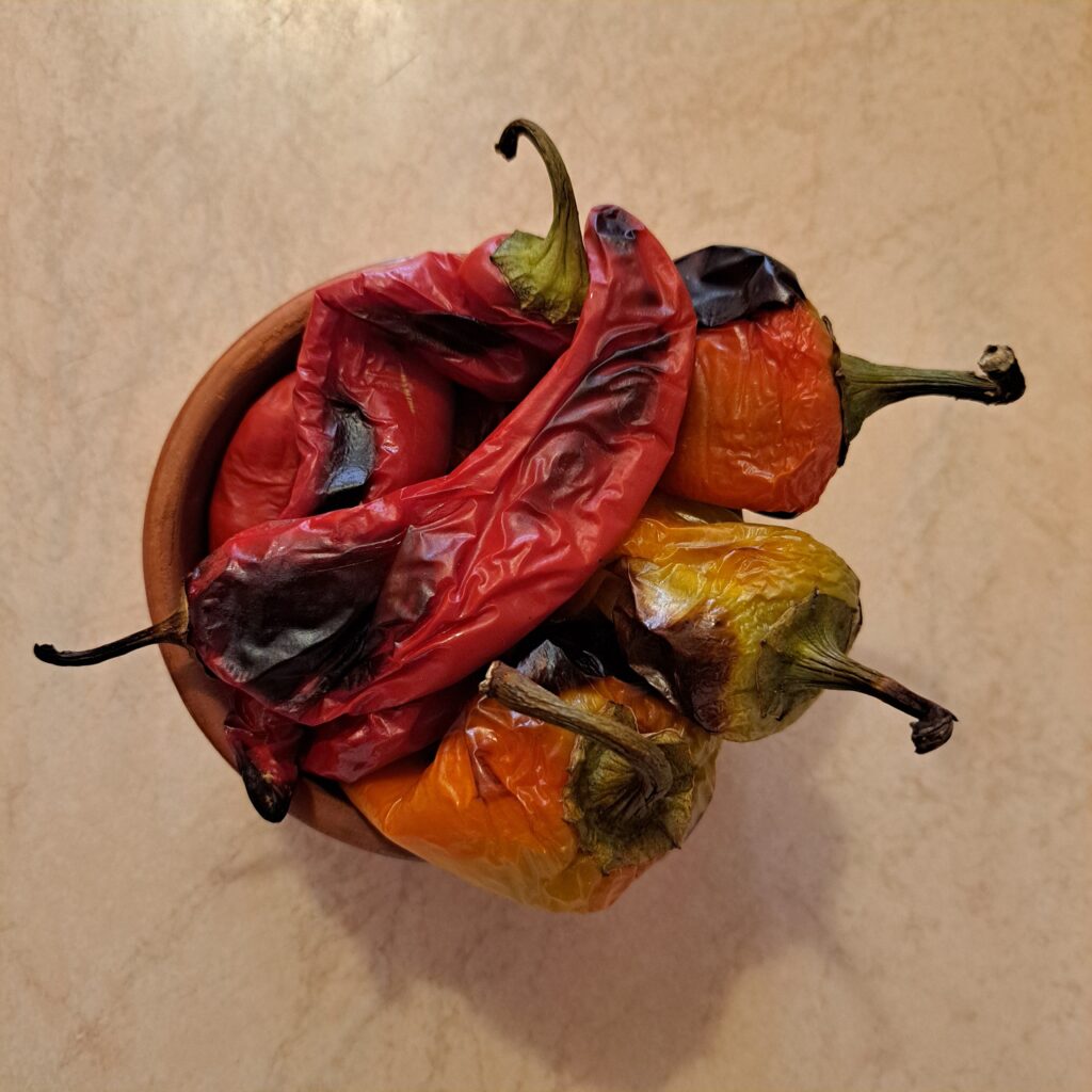 Whole red peppers roasted on a baking tray, ready to peel, seed, and chop for the filling.