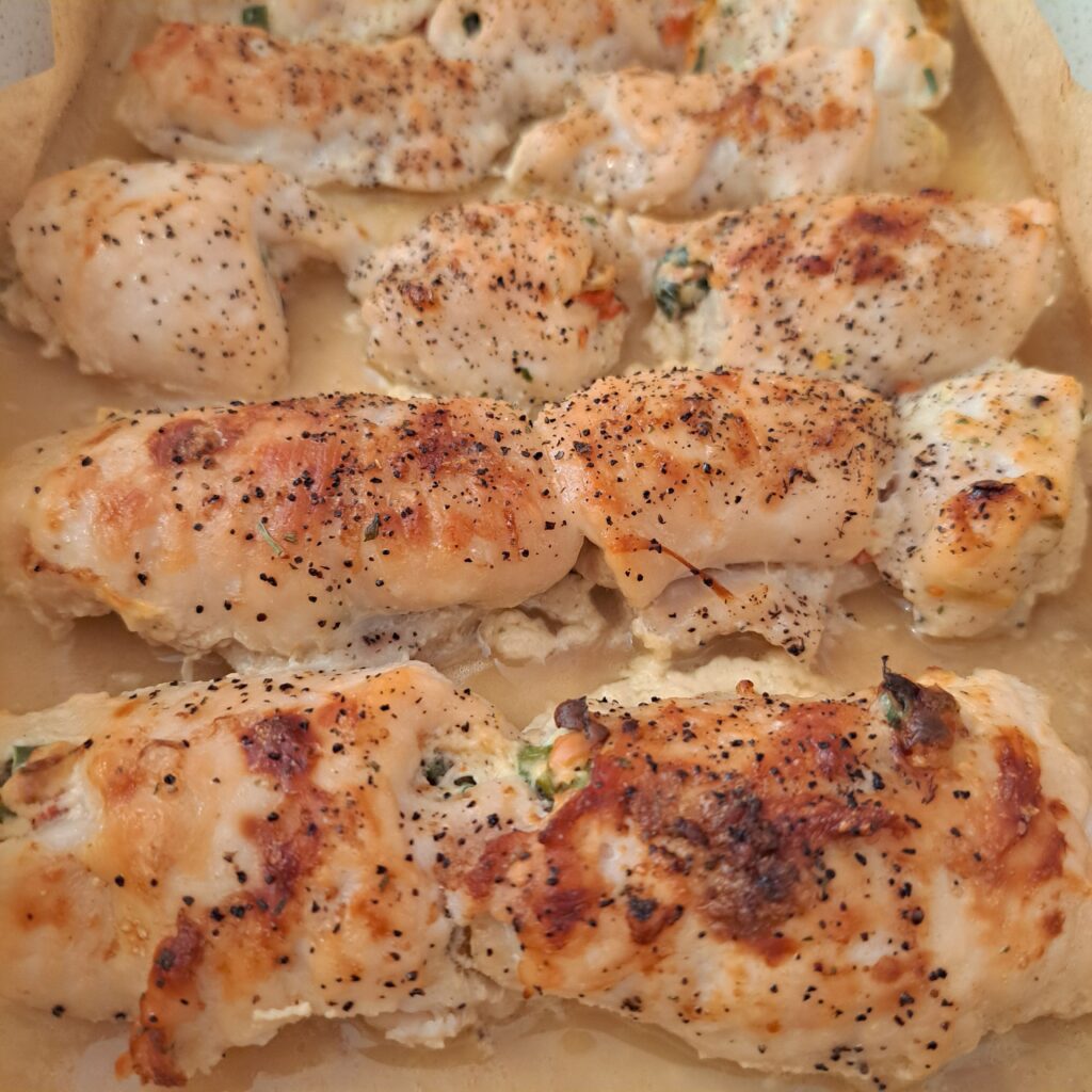 Golden mini rolled chicken bites baked in a tray, showing the filling peeking out.