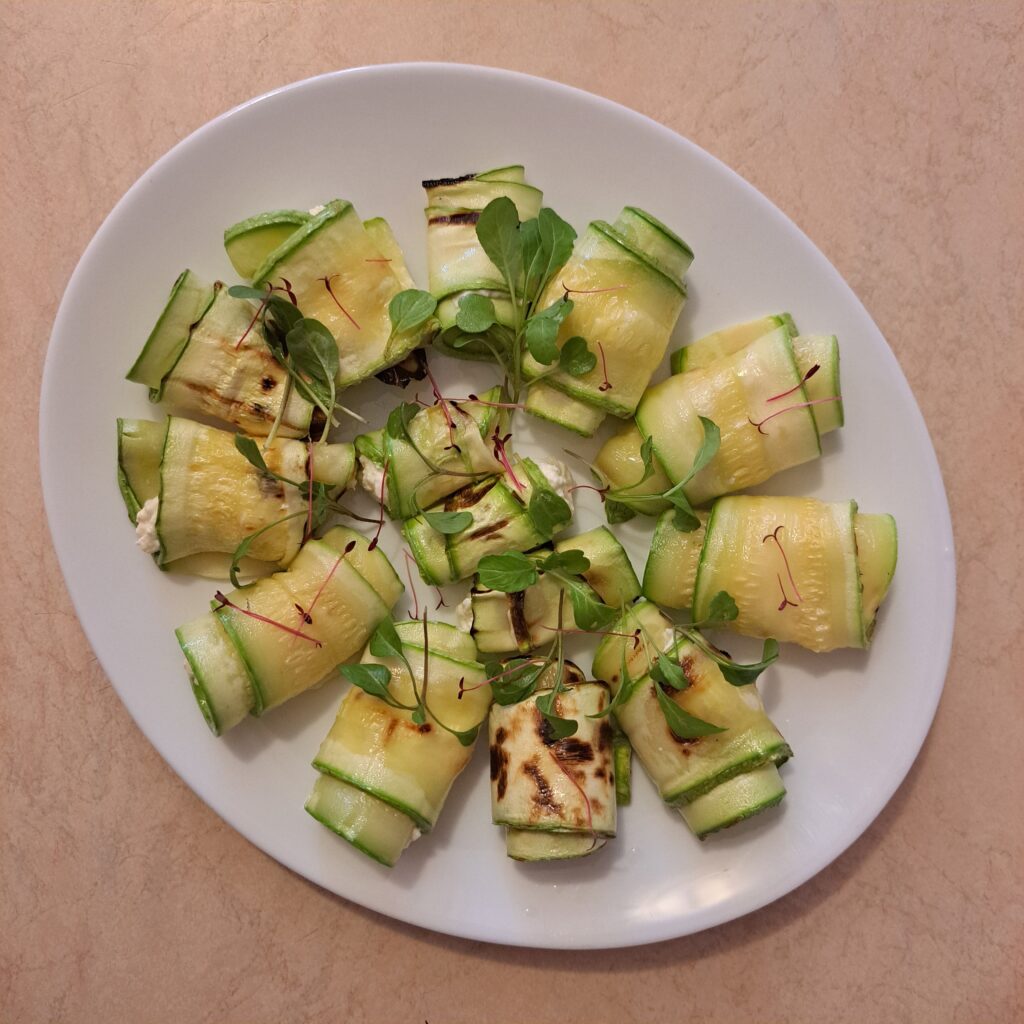 Grilled zucchini rolls decorated with arugula and amaranth microgreens.