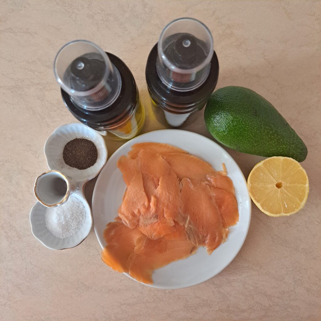 Avocado, smoked salmon, lemon, olive oil, salt, and pepper on table.