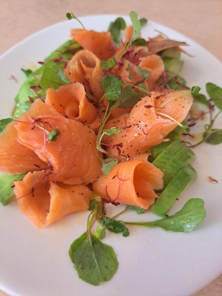 Side view of avocado slices with smoked salmon and microgreens on plate.