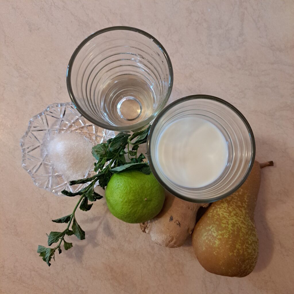Fresh ingredients on a kitchen table: pear, ginger, half lime, vanilla, yogurt, and water.