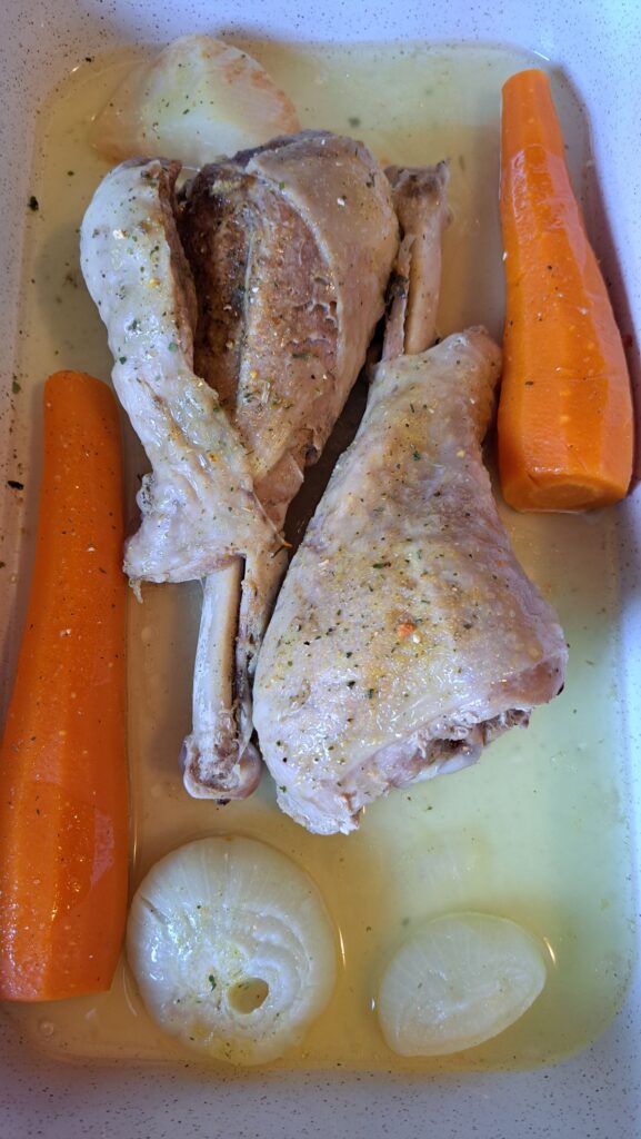 Turkey drumsticks and boiled vegetables placed in a baking tray with cooking water.