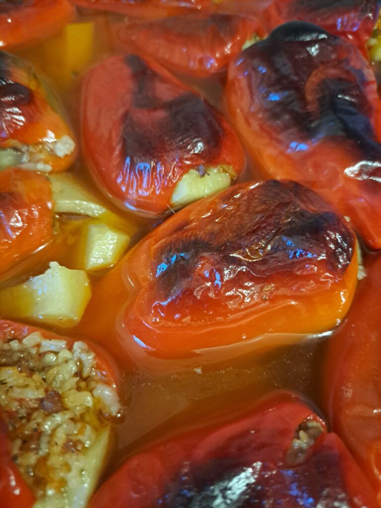 Baked stuffed red peppers filled with rice and pork in a baking dish.