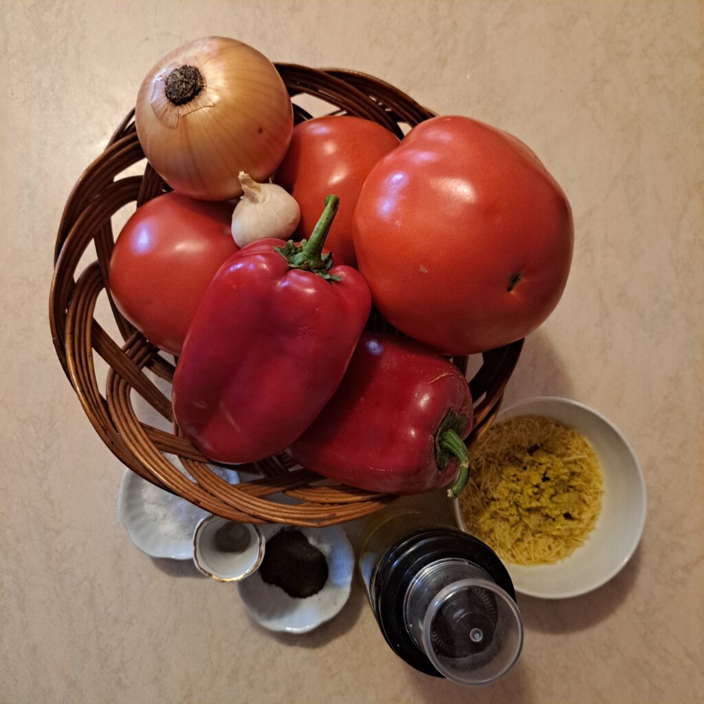 Whole red peppers, tomatoes, onion, garlic, oil, salt, and black pepper on a table.