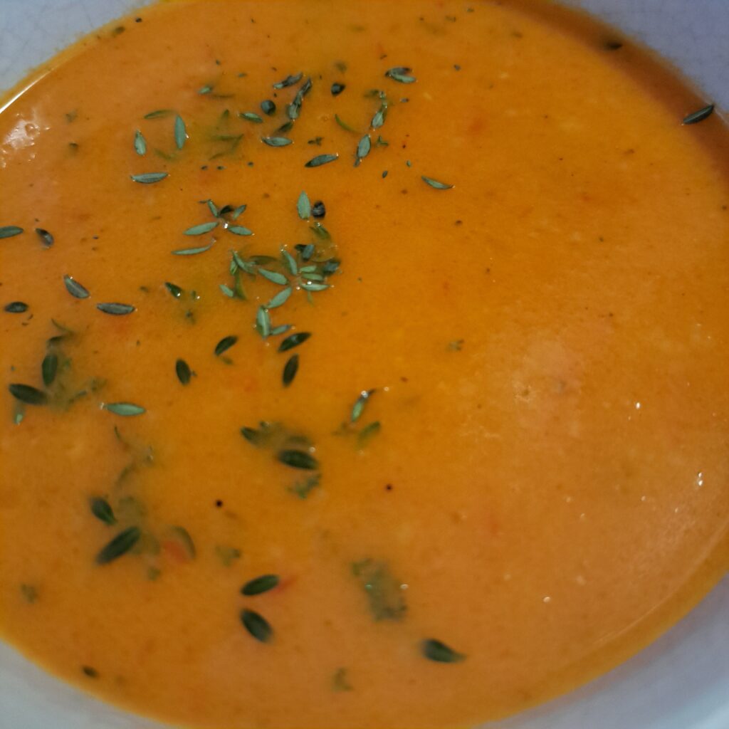 Close view of tomato and red pepper soup in a bowl with thyme decoration.