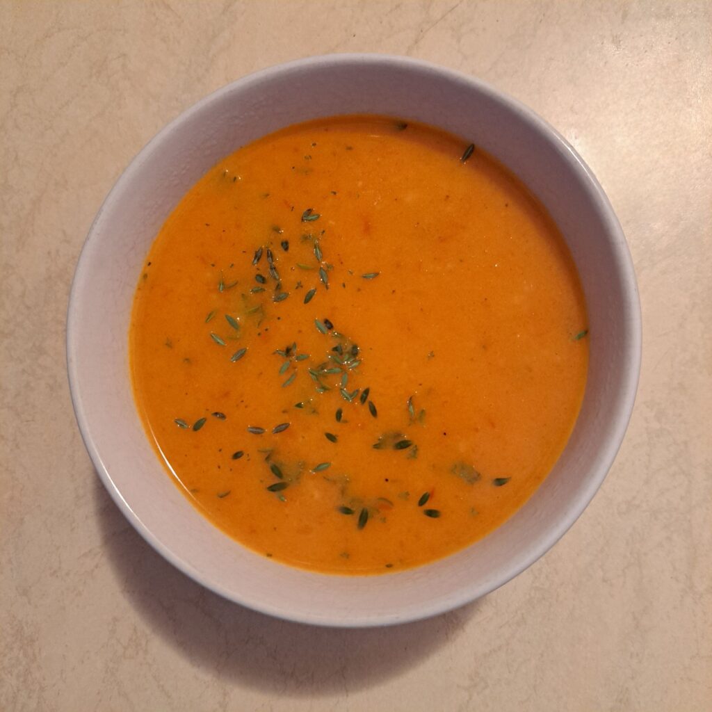 Bowl of tomato and red pepper soup with herbs garnished with thyme leaves.