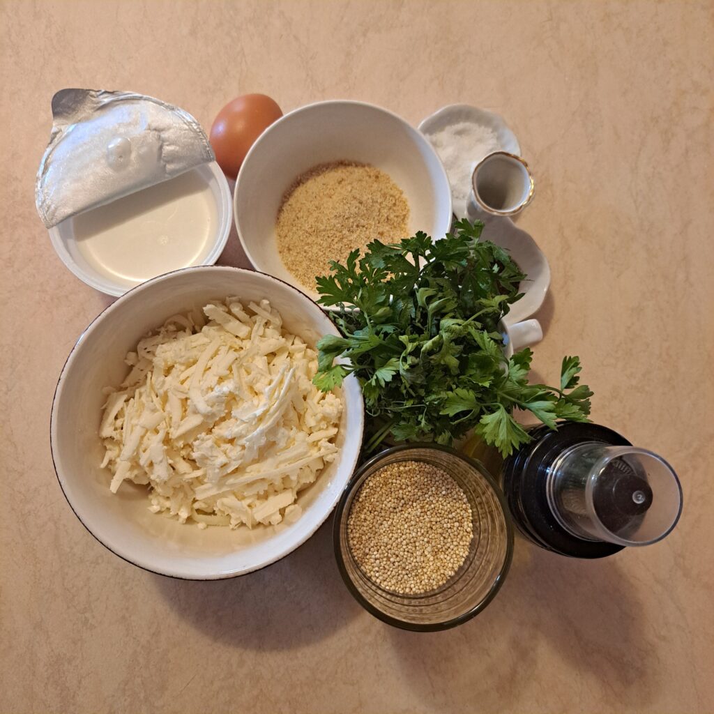 Quinoa, grated cheese, cream cheese, egg, breadcrumbs, parsley, salt, and pepper on a kitchen table.