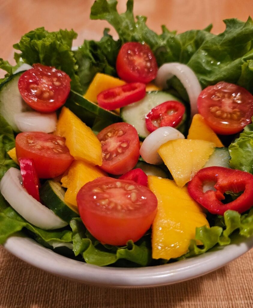 Close-up view of mango cucumber garden salad showing diced mango, cucumber, cherry tomatoes, onion, and red bell pepper in crisp greens.