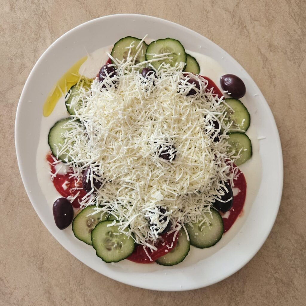 Grated white cheese sprinkled over the salad with cucumbers, tomatoes, and olives.