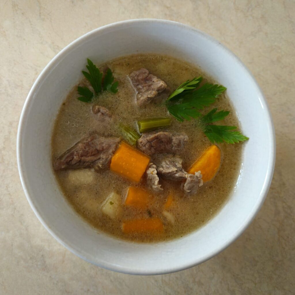 Served beef parsnip celery soup in a white round deep bowl, garnished with fresh parsley leaves.