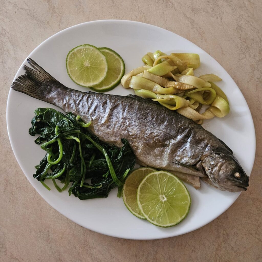 Served baked trout with spinach and zucchini on a white plate, decorated with thin slices of lime.
